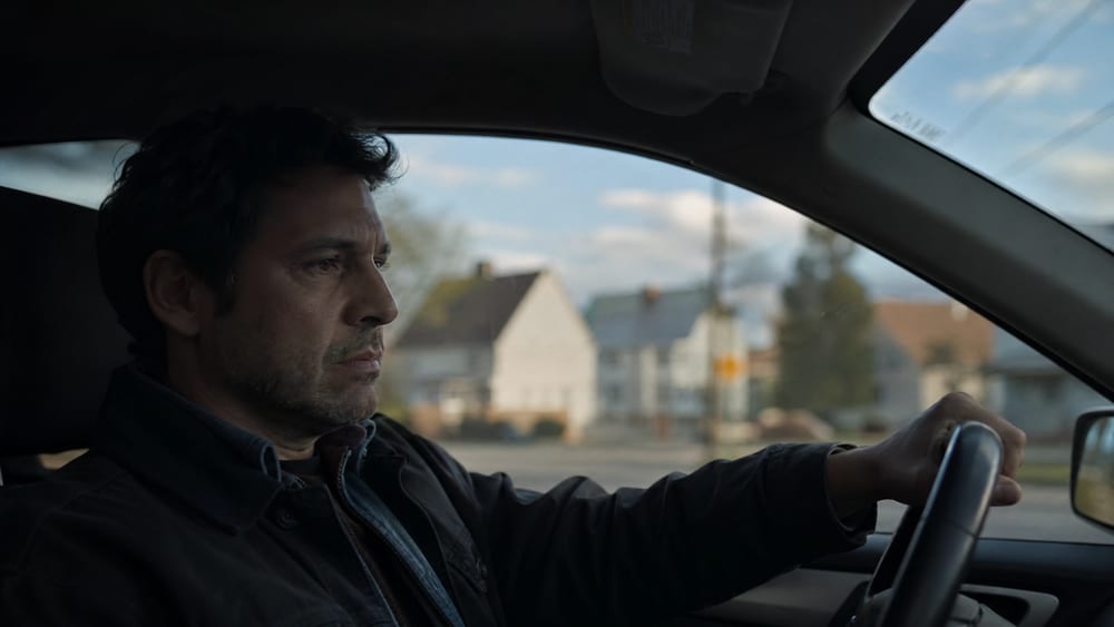 A man driving alone, looking pensive and far away, a good man who has quietly stopped sharing what's on his mind