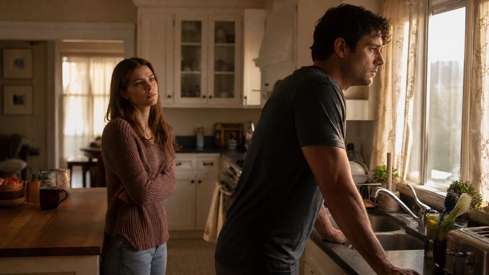 A couple standing in the kitchen facing each other in a tense conversation, his words saying he's fine when nothing is fine
